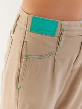 Pantalón largo color beige, tipo baggy, con costuras en verde y etiqueta turquesa en la parte trasera.