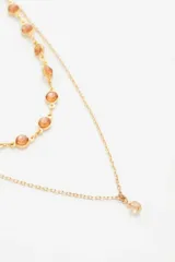 Collar doble dorado, uno con cadena de eslabones grandes y dijes de piedra color ámbar, y otro con cadena fina y dije colgante de cristal facetado.