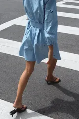 Vestido corto celeste con bordados calados, escote en V, mangas 3/4 abullonadas con elástico y cinturón con hebilla redonda de madera. Cierre frontal con botones.