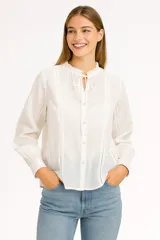 Blusa blanca de manga larga con cuello mao con lazo y cierre frontal con botones.