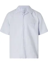 Camisa celeste de manga corta con cuello cubano, cierre frontal con botones y bolsillo de parche en el pecho.