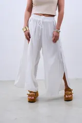 Pantalón blanco de tela fluida con cintura elastizada y cordón ajustable. Presenta aberturas laterales amplias desde la cintura hasta el ruedo.