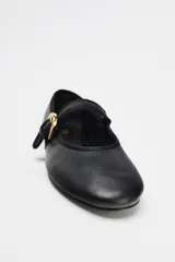 Zapato plano tipo bailarina color negro, confeccionado en piel, con tira delantera con hebilla metálica ajustable y acabado en punta redonda.