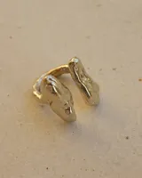Anillo de diseño orgánico y macizo, realizado artesanalmente en bronce. Presenta una estructura abierta con dos piezas de forma irregular y textura rugosa.