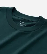 Remera de algodón color verde oscuro, corte relaxed, cuello redondo y manga corta. Presenta un pequeño estampado en el pecho con el texto "N.Y.U.S" en blanco y dos franjas blancas horizontales en cada manga.