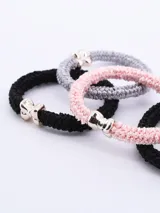 Pack de cuatro coleros elásticos para el pelo, en colores negro, gris y rosa, con aplique metálico plateado en forma de moño.