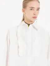 Camisa de poplín blanca, con alforzas y volados en el delantero, de corte largo hasta la cadera y mangas largas.