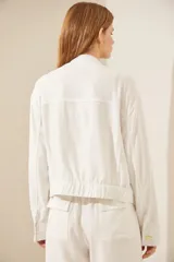 Chaqueta bomber color beige con cuello mao, cierre frontal con botones dorados, bolsillos de parche con solapa y bordado en el pecho. Puños y cintura elastizados.