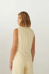 Chaleco color crema con cuello alto y cierre frontal con cremallera. Diseño con alforzas verticales en la parte superior delantera y trasera.