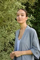 Bata tipo kimono de algodón color blanco hueso, con textura acanalada vertical. Presenta un cruce frontal asegurado con un lazo a la cintura y mangas anchas de largo al codo.