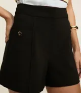 Short color beige de cintura alta, confeccionado en tejido plano con estructura sastre, con bolsillos laterales con tachuelas metalizadas.