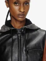 Chaqueta de cuero de oveja negra con mangas marrones y capucha de algodón gris extraíble con cordones. Cierre frontal con cremallera, cuello alto minimalista, puños con cremallera y forro interior.