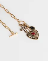 Collar corto dorado con cadena de eslabones grandes y cierre de gancho. Incluye dijes colgantes: corazón dorado liso, cuenta negra, cruz con strass y corazón dorado con corazón rojo en el centro.