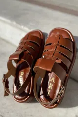Sandalias bajas de cuero color suela, con tiras anchas entrecruzadas y hebilla lateral.