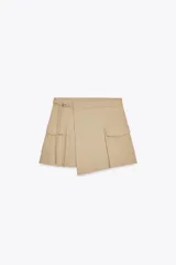 Falda pantalón color beige, de tiro alto, con bolsillos laterales tipo cargo, detalle de tablas y cierre lateral con cremallera oculta y trabilla con hebilla metálica.