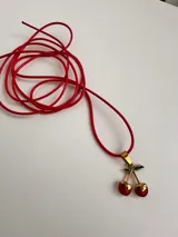 Gargantilla con cordón rojo y dije de cerezas rojas con detalles dorados y hojas verdes.