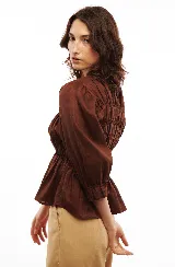 Blusa marrón de lino liviano con escote en V, abotonadura frontal y mangas 3/4 con puño. Diseño con frunces que generan un efecto entallado en la parte superior y amplio en el ruedo.