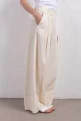 Pantalón de vestir color crema, de tiro medio y corte ancho. Presenta pinzas en la parte delantera y largo hasta los tobillos.