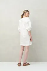 Vestido corto blanco de algodón con bordado floral en relieve, escote redondo con abotonadura frontal y mangas amplias.