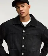 Campera masculina de jean negro con efecto desteñido, modelo boxy, con cuello solapa, manga larga con puño abotonado, cierre frontal con botones, bolsillos grandes y recortes.