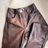 Pantalón de cuero negro, de corte recto y tiro alto, con bolsillos delanteros y traseros.