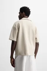 Polo color beige de corte relaxed fit, confeccionado en tejido interlock de algodón con elasticidad. Tiene cuello solapa y cierre frontal de cremallera.
