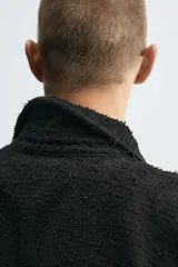 Camisa negra de denim de algodón con textura irregular, corte relaxed fit, cuello solapa, manga larga con puños abotonados y cierre frontal con botones.