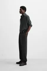 Pantalón negro de corte amplio confeccionado en tejido con mezcla de viscosa. Presenta cintura elástica, pliegues en la parte delantera, bolsillos laterales y traseros de vivo. Cierre frontal con cremallera y gancho metálico oculto.