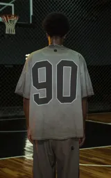 Remera de manga corta y cuello redondo, calce oversize, color marrón oscuro con efecto batik/lavado. Presenta un pequeño bordado o aplique con la palabra "RAVERS" en el pecho.