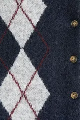 Saco corto de punto jacquard color azul marino con estampado de rombos en gris claro y líneas finas bordó. Tiene cuello redondo, cierre frontal con botones dorados y ribetes acanalados en puños y bajo.