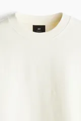 Remera color crema de punto de algodón pesado, con cuello redondo ribeteado, hombros caídos, bajo recto y corte oversized.