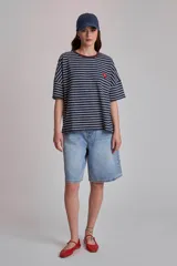 Remera de corte holgado con estampado de rayas horizontales azul marino y blancas, cuello redondo con ribete marrón y logo rojo bordado en el pecho.