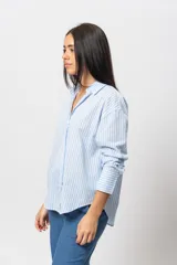 Camisa celeste a rayas verticales blancas, de corte recto y mangas largas con puños abotonados.
