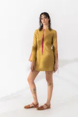 Vestido corto color mostaza con escote redondo y mangas largas acampanadas. Presenta detalle de tiras fucsias en escote y mangas.