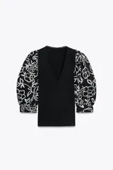 Top negro con escote en pico, detalle de fornitura y mangas abullonadas al codo con bordado de flores blancas.