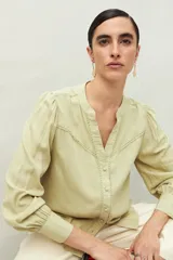 Camisa celeste de manga larga con cuello redondo y escote en V. Presenta detalles de pasamanería en el frente y las mangas, y botones forrados al tono. De corte fluido.