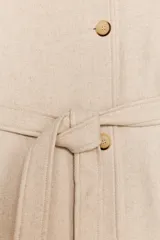 Abrigo largo color beige confeccionado en hilatura con lana. Tiene cuello subido, manga larga con trabillas, bolsillos laterales y cinturón ajustable con lazada. El cierre frontal es cruzado con botones.