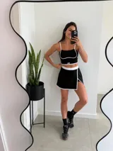 Conjunto deportivo negro con detalles en blanco, compuesto por un top corto con tirantes finos y una minifalda con short incorporado y abertura lateral.