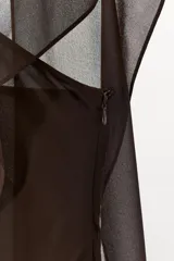 Vestido largo marrón con escote asimétrico y tirante ancho. Tiene una capa de tejido transparente a tono sobre el hombro y abertura lateral en el ruedo.