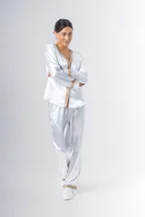 Pijama blanco de satén elastizado, compuesto por una camisa de manga larga con escote en V, abotonada adelante y con puntilla en escote y puños, y un pantalón recto con bolsillos laterales, elástico en la cintura y puntilla en el ruedo.