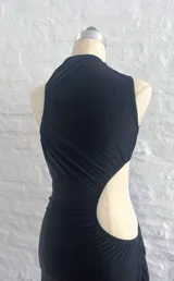 Vestido largo negro con cuello alto, sin mangas y abertura en la cintura.