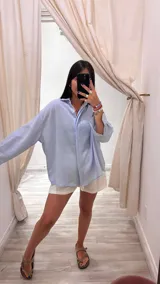 Camisa color beige claro con textura brillante, cuello clásico, cierre frontal con botones y mangas largas con puños abotonados.