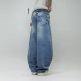 Jean de hombre, color celeste desgastado, corte ultra ancho (baggy) y tiro alto. Presenta un parche de cuero marrón con logo en el reverso de la cintura y un estampado circular blanco en el bolsillo trasero derecho.