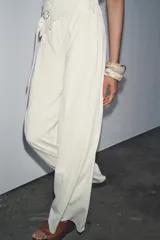 Pantalón de tiro alto color crema, de corte palazzo, con cinturón ancho de tela con hebilla metálica.