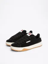 Zapatillas Tommy Jeans de corte bajo, color negro, con exterior de ante, interior de poliéster y suela de goma color caramelo. Presentan un panel a contraste en el talón, logo de Tommy Jeans en la lengüeta y etiqueta de la marca en el lateral.