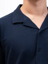 Camisa de manga corta color azul marino, confeccionada en tejido piqué de algodón. Presenta cuello cubano y cierre frontal de botones. Incluye un bolsillo de parche en el pecho izquierdo.