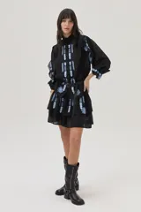 Minivestido negro con bordados florales celestes, cuello alto, mangas largas abullonadas con volados, falda corta con volados y cinturón fino negro.