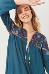 Vestido azul petróleo con bordados en cuello y mangas, escote en V con cordones y mangas largas abullonadas.