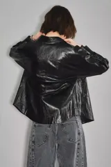 Campera negra de cuero sintético con acabado brillante, cuello camisero, cierre frontal con botones y dos bolsillos delanteros con solapa.