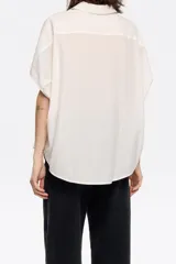 Camisa corta color crema de 100% algodón con cuello camisero y manga corta murciélago. Cierre frontal con botonadura.